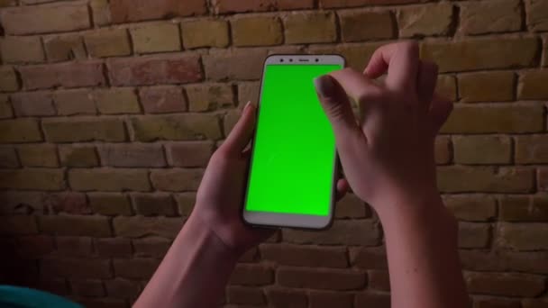 Ritratto ravvicinato delle mani femminili che toccano e scorrono sullo schermo verde dello smartphone sullo sfondo della parete in mattoni . — Video Stock