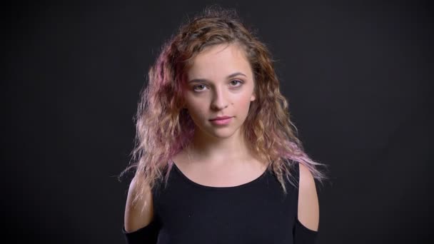 年轻女孩的肖像与粉红色的头发平静地观看成相机在黑色背景. — 图库视频影像
