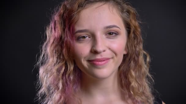 Portrait of young caucasian girl with pink hair watching into camera and humbly smiling on black background. — Stock Video