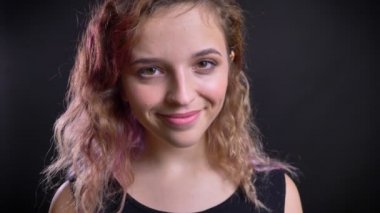Sakince gülümseyerek ve siyah arka plan üzerine kamera içine kafasını sallayarak sevimli genç beyaz kız portresi yakın çekim.
