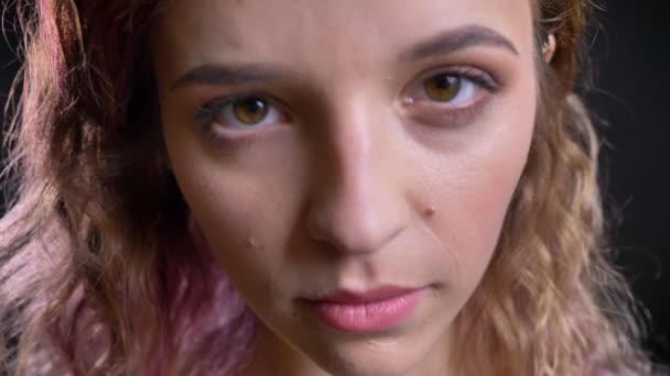 Close-up portrait of young caucasian girl shrilly watching into camera on black background. — Stock Video