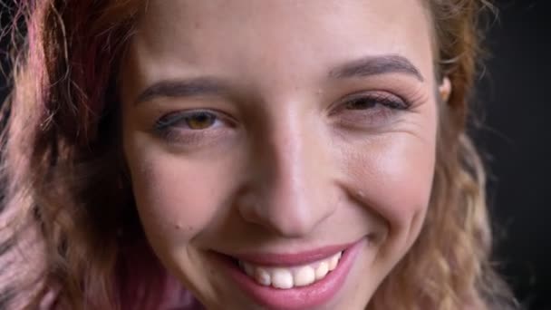 Close-up portrait of cute young caucasian girl shyly smiling into camera on black background. — Stock Video