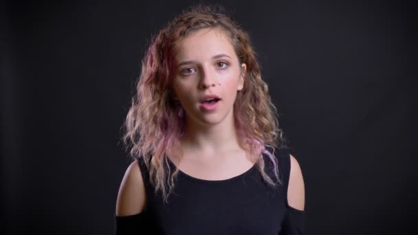 Портрет молодої білої дівчини з рожевим волоссям, що дивиться в камеру з розвагами на чорному тлі . — стокове відео