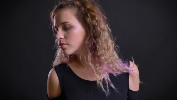 Porträt eines jungen kaukasischen rosafarbenen Mädchens, das auf schwarzem Hintergrund kokett posiert und ihre Haare in die Kamera schüttelt. — Stockvideo
