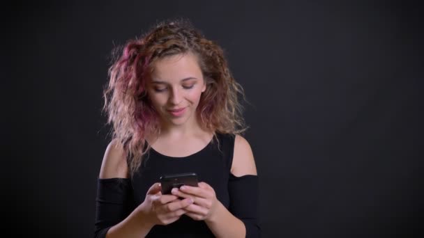 Портрет молодої кавказької дівчини з рожевим волоссям, що дивиться в її смартфон, здивується і радіє на чорному тлі . — стокове відео