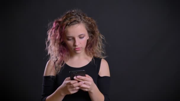 Retrato de chica caucásica joven con el pelo rosa mirando en su teléfono inteligente se sorprende y molesta en el fondo negro . — Vídeo de stock