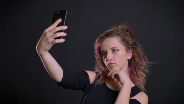 Porträt eines jungen kaukasischen Mädchens mit rosa Haaren, das Selfie-Fotos mit dem Smartphone auf schwarzem Hintergrund macht. — Stockvideo