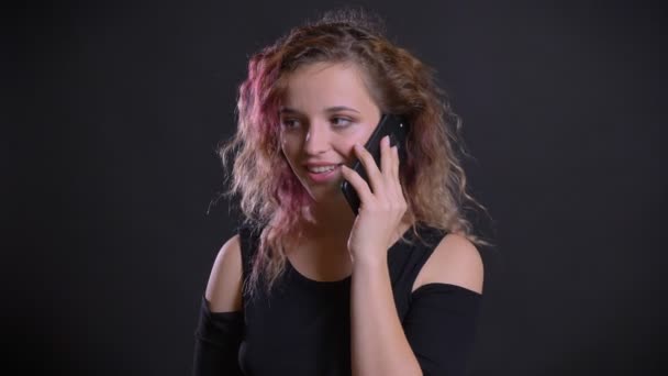 Retrato de chica caucásica joven con el pelo rosa felizmente hablando en el teléfono celular sobre fondo negro . — Vídeos de Stock