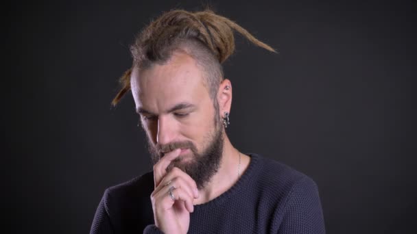 Close-up portrait of freaky man with dreadlocks and piercing thoughtfully touching his beard gets insight on black background. — Stock Video