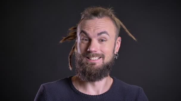 Porträt eines ausgeflippten kaukasischen Mannes mit Dreadlocks und Piercing, der positive Belustigung und Glück auf schwarzem Hintergrund zeigt. — Stockvideo