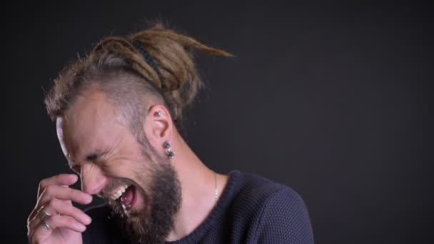 Porträtt av freaky kaukasiska man med dreadlocks och piercing skrattar glatt på svart bakgrund. — Stockvideo