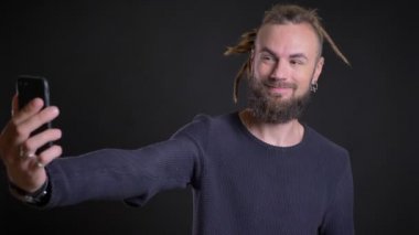 Dreadlocks ve selfie-fotoğrafları yapma piercing olan garip beyaz adam portresi siyah arka plan üzerine smartphone kullanarak