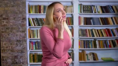 Arka plan sevinçle kitap telefonda konuşurken piercing ile sarışın beyaz genç kız portresi raflar.