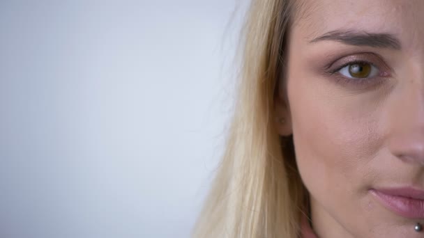 Close-up semi-retrato de jovem mulher loira caucasiana assistindo agradavelmente e diretamente na câmera em fundo cinza . — Vídeo de Stock