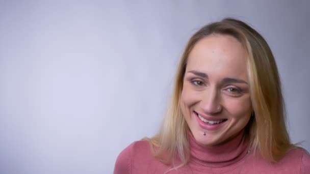 Retrato de la joven rubia caucásica riendo tímidamente en la cámara sobre fondo gris . — Vídeos de Stock