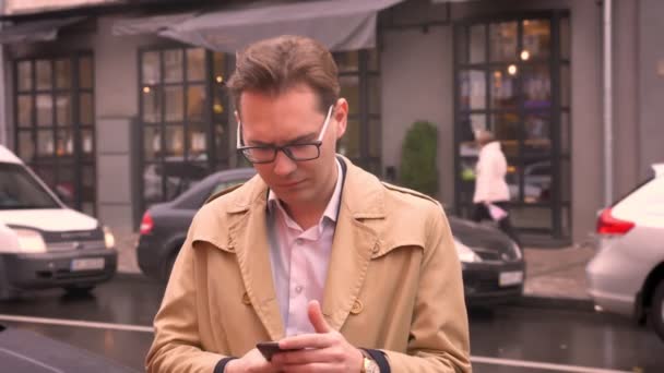 Hombre caucásico adulto saca el teléfono del bolsillo y recibe notificación sobre buenas noticias usando abrigo y de pie en la calle al aire libre — Vídeo de stock