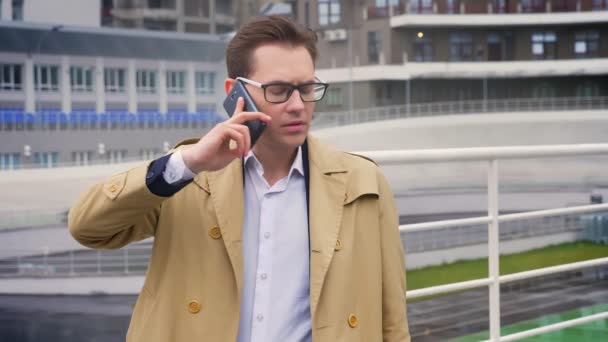 Привабливий молодий кавказький чоловік розмовляє по телефону, стоячи біля стадіону в серйозному і концентрованому настрої — стокове відео