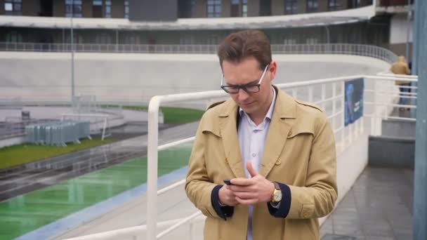 Primer plano retrato de hombre caucásico atractivo comprobando el teléfono y conseguir feliz y sorprendido de pie al aire libre en la ciudad — Vídeo de stock