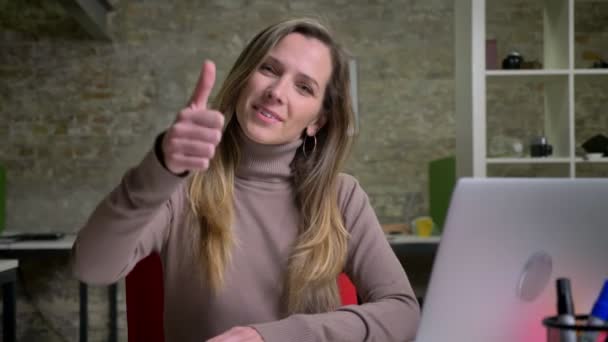 Retrato de close-up de trabalhadora de escritório branca na frente do laptop sorrindo puxando o braço e mostrando o polegar para cima — Vídeo de Stock