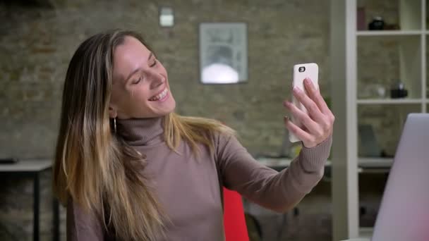 Closeup πορτρέτο του ελκυστική γυναίκα υπάλληλος έχοντας μια κλήση βίντεο, κουνώντας Γεια και χαμογελά στο χώρο εργασίας — Αρχείο Βίντεο