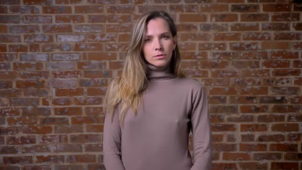 Closeup portret van verbluffende Kaukasische vertrouwen vrouw kijkt van de camera in een serieuze bui met de bakstenen muur op de achtergrond — Stockvideo