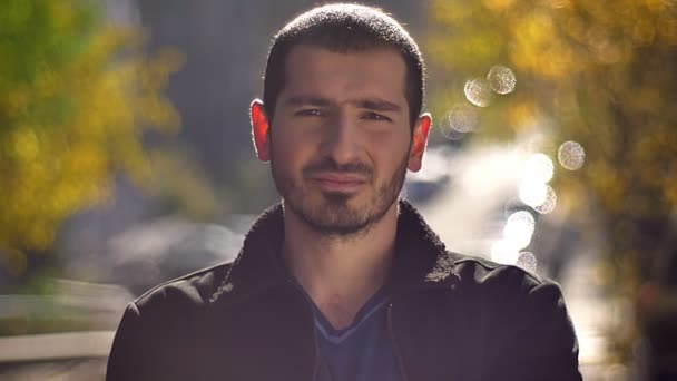 Portrait of young caucasian man smiling sincerely into camera on autumnal street background. — Stock Video