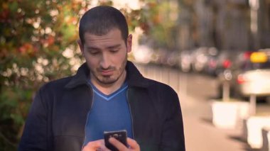 Beyaz adam memnuniyetini sokak arka plan üzerinde öfke duyguları değiştirme smartphone içine izlerken.