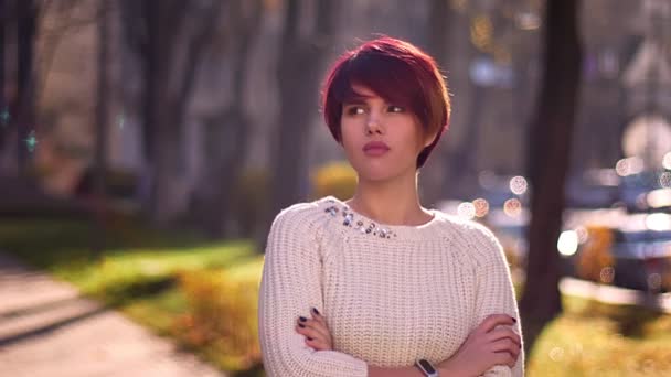 Portrait de jeune fille aux cheveux roses caucasiens avec les bras croisés regardant calmement dans la caméra dans le parc . — Video