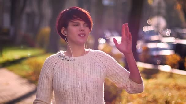 Портрет молодой розововолосой девушки, слушающей музыку в наушниках и танцующей с восторгом на фоне осеннего парка . — стоковое видео