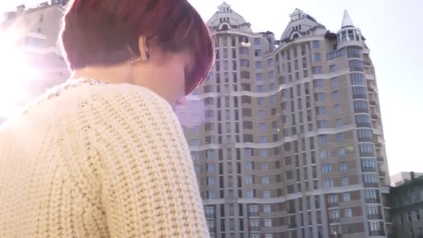 Zoom posteriore ritratto di bella ragazza dai capelli rosa in piedi vicino ringhiera e tristemente guardando sulla vista urbanistica . — Video Stock
