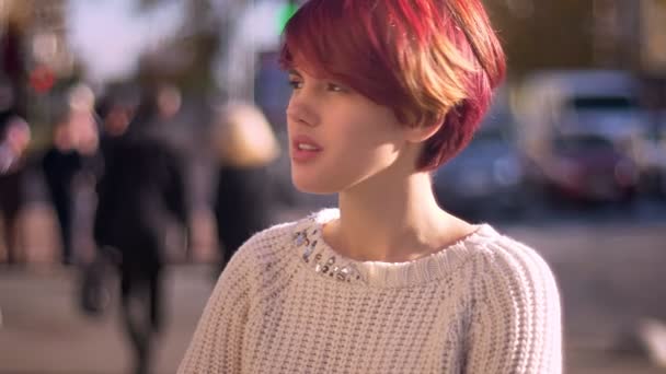 Porträtt av unga kaukasiska rosa hår flicka leende ödmjukt in kameran och tittar på gatan suddig bakgrund. — Stockvideo