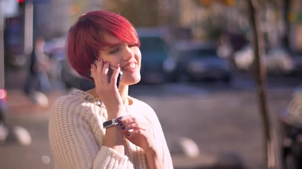 Retrato de la feliz chica de pelo rosa bonita hablando en el teléfono celular sobre fondo borroso de la calle . — Vídeos de Stock