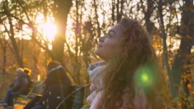 Bankta oturan ve mutlu bir şekilde smartphone ve yukarı doğru Sonbahar Park izlerken beyaz kıvırcık saçlı kadın portresi.