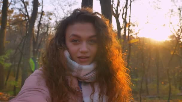 Auto-video de una joven caucásica de pelo rizado haciendo selfies-fotos en el parque otoñal . — Vídeos de Stock