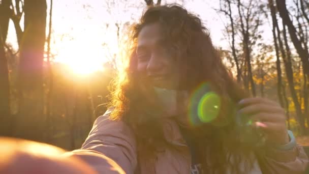 Self-video of smiling caucasian curly-haired woman in sunshine talking in videochat in autumnal park. — Stock Video