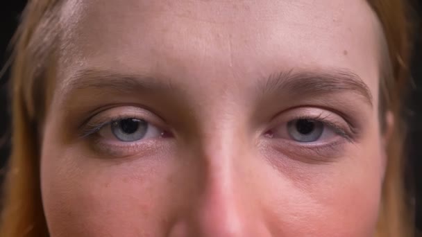 Retrato ocular de cerca de una mujer vestida formalmente mirando tranquilamente a la cámara sobre un fondo negro . — Vídeos de Stock