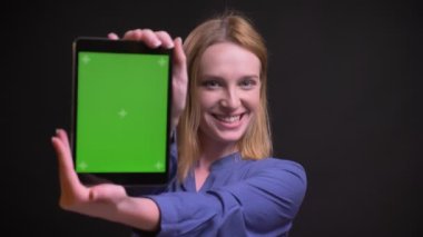 Genç sarışın beyaz kadın mutlu yeşil gösterilen portresi görüntülemek için kamera siyah arka plan üzerine tablet.