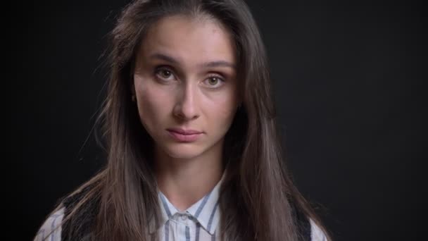 Portrait of young caucasian long-haired woman negatively turns her head watching into camera on black background. — Stock Video