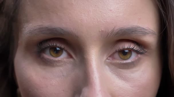 Close-up eye-portrait of young caucasian long-haired woman watching calmly into camera on black background. — Stock Video