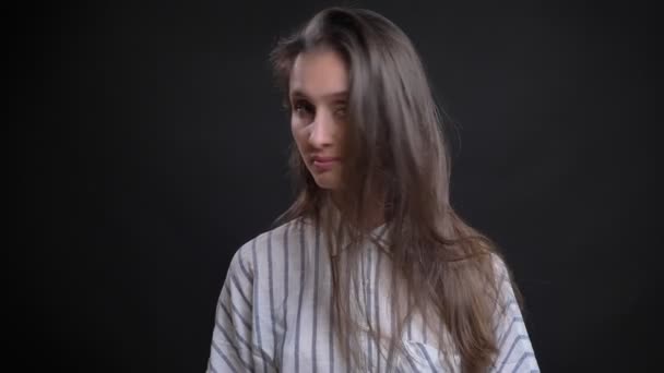 Retrato de una joven caucásica de pelo largo girando lentamente la cabeza y mirando tranquilamente a la cámara sobre fondo negro . — Vídeos de Stock