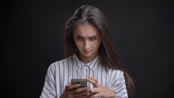 Portret van mooie Kaukasische langharige vrouw kijken in smartphone en lachen op zwarte achtergrond. — Stockvideo