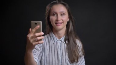 Siyah arka plan üzerine smartphone kullanarak görüntülü sohbet konuşan genç beyaz uzun saçlı kadın portresi.