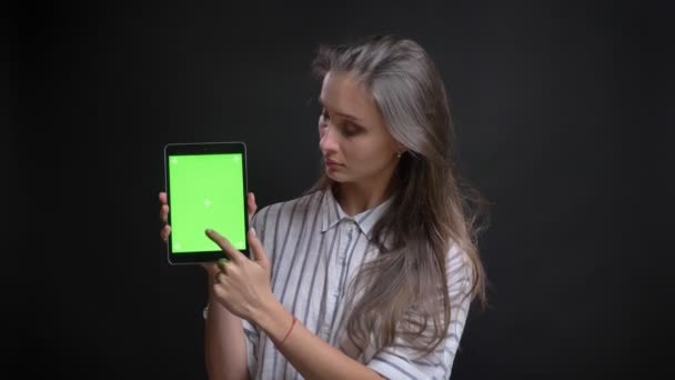 Retrato de una hermosa mujer caucásica de pelo largo mostrando la pantalla verde de la tableta a la cámara sobre fondo negro . — Vídeo de stock