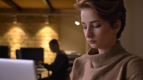 Close-up portret van korthaar jongedame aandachtig werken met laptop in kantoor. — Stockvideo