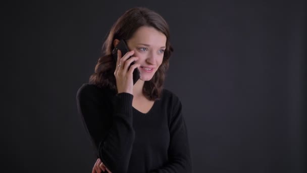 Portrét mladé atraktivní kavkazské dlouhé vlasy dívka s úsměvem mluví na smartphone na černém pozadí. — Stock video