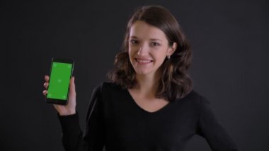 Genç beyaz uzun saçlı kız gülümseyerek smartphone kamera için yeşil ekran siyah arka plan üzerinde gösterilen portresi.