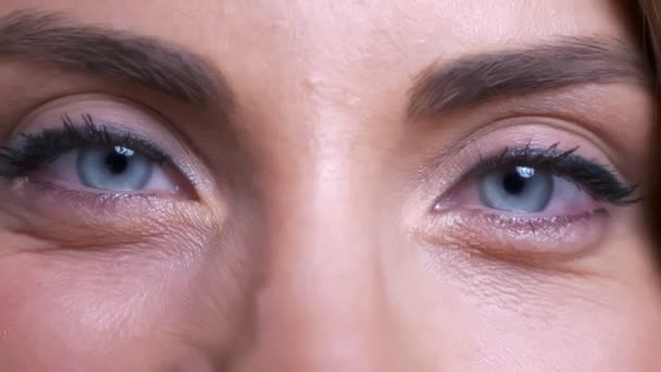 Крупним планом портрет красивих молодих кавказьких жіночих блакитних очей дивиться прямо на камеру з усміхненим виразом обличчя — стокове відео