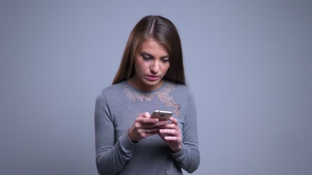 Retrato de close-up de jovem caucasiano feminino navegando casualmente no telefone girando e olhando para a câmera sorrindo — Vídeo de Stock