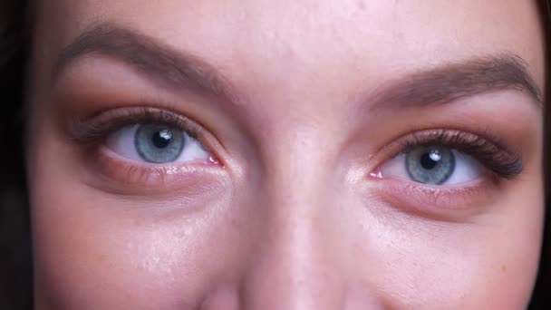 Retrato de cerca de hermosos ojos azules femeninos caucásicos jóvenes mirando directamente a la cámara con expresión facial sonriente — Vídeo de stock