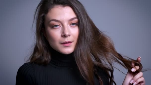 Primer plano de impresionante modelo femenina bastante caucásica jugando con su pelo posando y sonriendo a la cámara — Vídeos de Stock